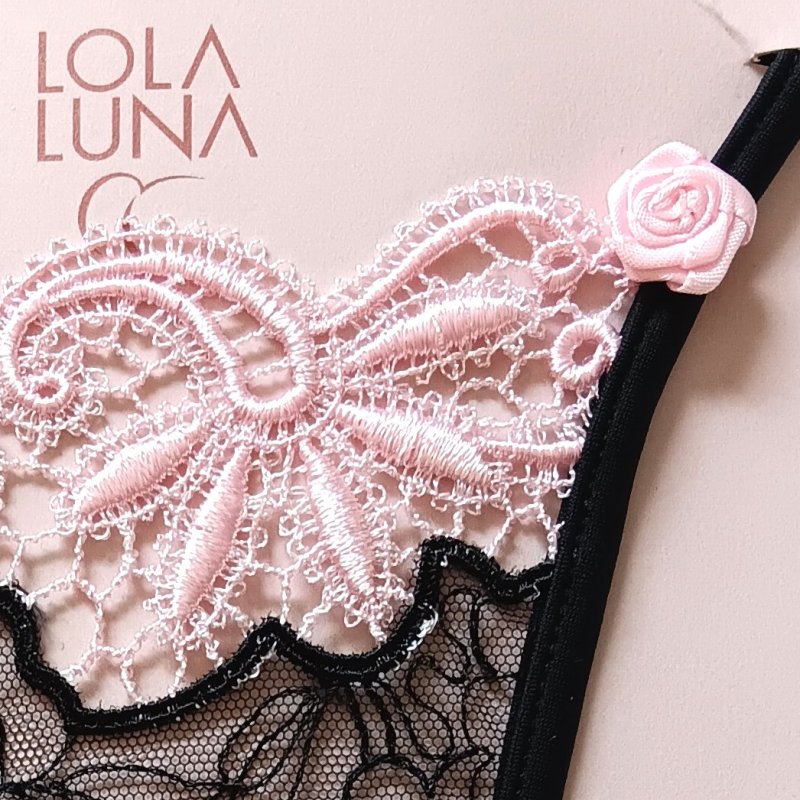 Lingerie féminine : mini string noir ouvert, détails en dentelle bicolore noire et rose, agrémenté d’un bijou cœur central.