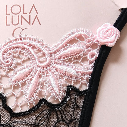 Lingerie féminine : mini string noir ouvert, détails en dentelle bicolore noire et rose, agrémenté d’un bijou cœur central.